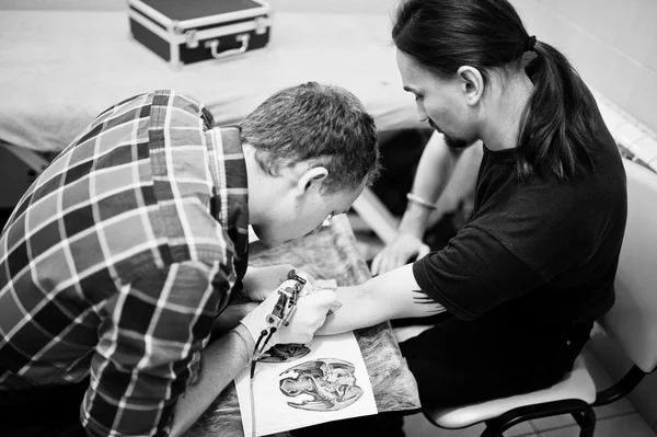 Il maestro del tatuaggio fa il tatuaggio per l'uomo dondolo al salone del tatuaggio — Foto Stock