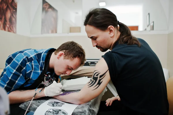 Il maestro del tatuaggio fa il tatuaggio per l'uomo dondolo al salone del tatuaggio — Foto Stock