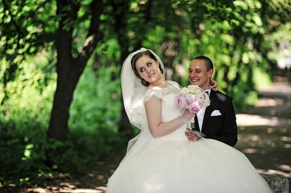 Fashionable wedding couple sitting on stone at park. — Stock Photo, Image