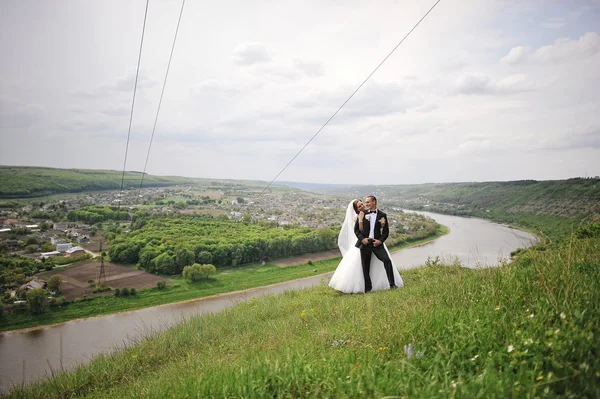 Prachtige bruidspaar op de heuvel met de rivier en mooie lan — Stockfoto