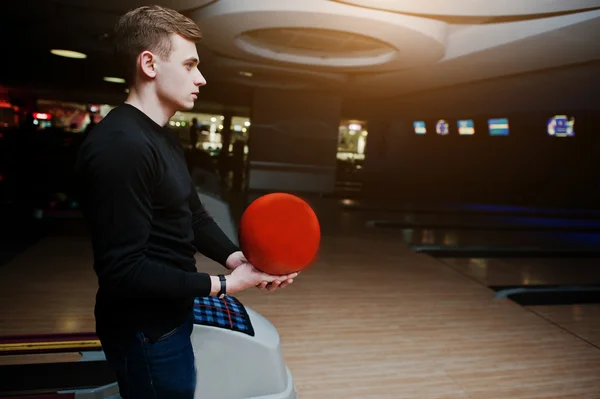 Jovem segurando uma bola de boliche contra becos de boliche — Fotografia de Stock