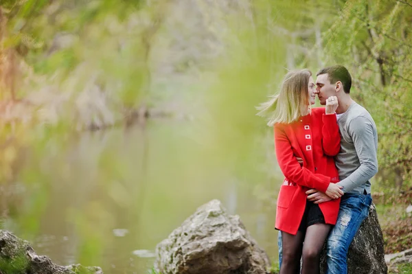 Glückliches Liebespaar sitzt und umarmt sich auf Stein im Park backgro — Stockfoto