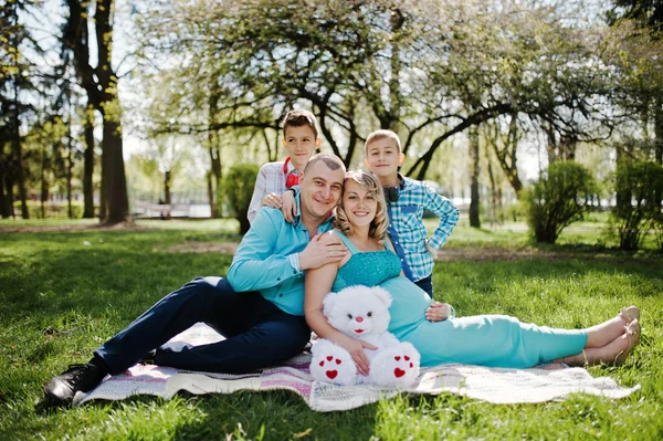 Gelukkige zwangere paar met twee zonen knuffelen en zittend op plaid — Stockfoto