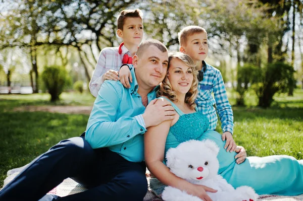 Gelukkige zwangere paar met twee zonen knuffelen en zittend op plaid — Stockfoto