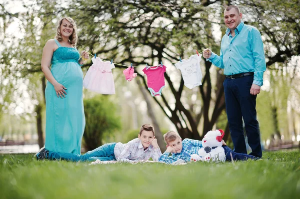 Feliz pareja embarazada con dos hijos sosteniendo la ropa de bebé de las niñas —  Fotos de Stock