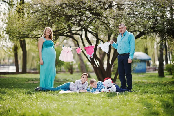 Glückliches schwangere Paar mit zwei Söhnen, die Mädchen Babykleidung halten — Stockfoto