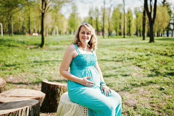 Gelukkige zwangere vrouw gekleed in een turquoise jurk zittend op een s — Stockfoto