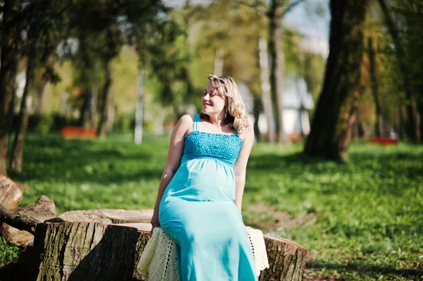 Happy pregnant woman dressed in a turquoise dress sitting on a s — Stock Photo, Image