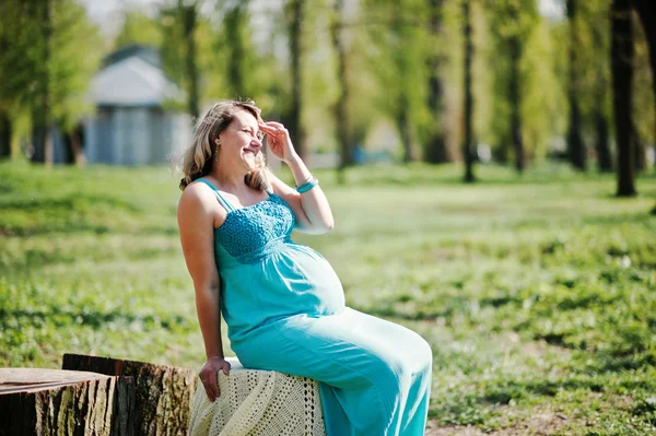 Feliz mujer embarazada vestida con un vestido turquesa sentado en una s —  Fotos de Stock