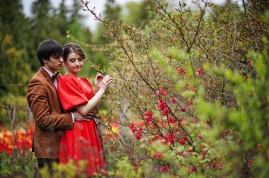 Çiçeklerle çalılıkların yanında birbirlerine sarılan çift. Ve şık adam