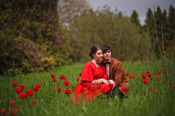 Pareja abrazándose en el amor en el campo de tulipanes rojo. Hombre con estilo en terciopelo — Foto de Stock