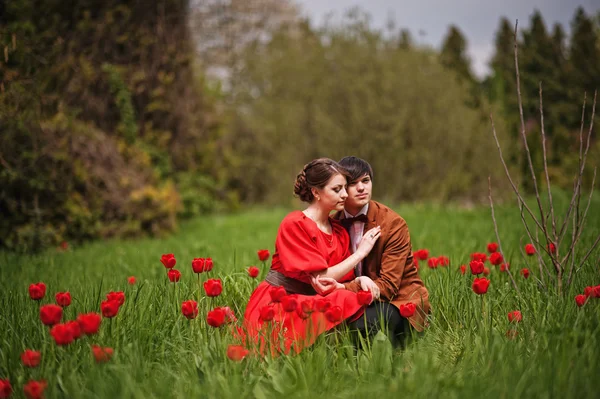 Pareja abrazándose en el amor en el campo de tulipanes rojo. Hombre con estilo en terciopelo — Foto de Stock