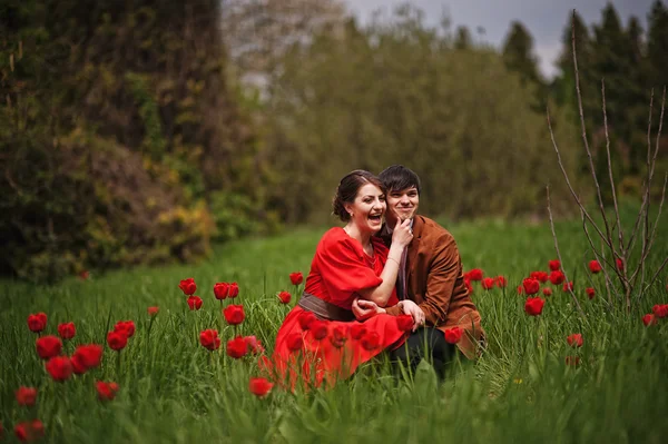 Pareja abrazándose en el amor en el campo de tulipanes rojo. Hombre con estilo en terciopelo — Foto de Stock