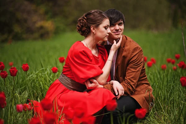 Pareja abrazándose en el amor en el campo de tulipanes rojo. Hombre con estilo en terciopelo — Foto de Stock