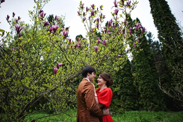 Pareja abrazándose en el amor cerca de magnolia árbol. Hombre con estilo en terciopelo —  Fotos de Stock