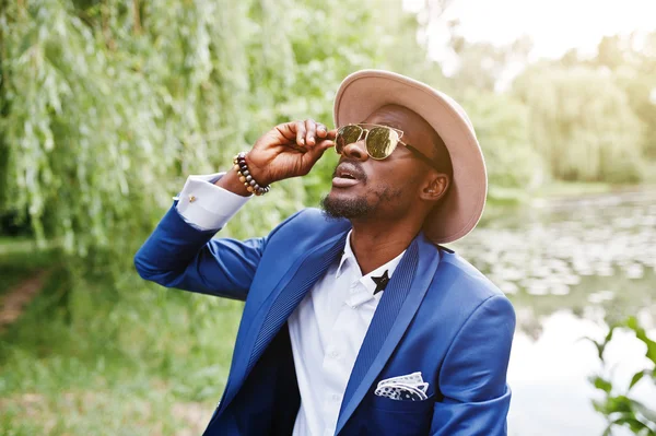 Portrait of stylish rich black man at blue jacket, hat and sungl