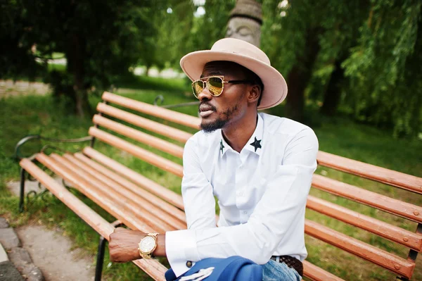 Gazdag fekete ember ül a padon arany napszemüveg és kalap — Stock Fotó