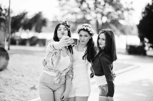Três meninas em shorts curtos e grinaldas na cabeça fazem selfie — Fotografia de Stock