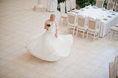 Muhteşem sarışın gelin kapalı büyük düğün salonu poz verdi.