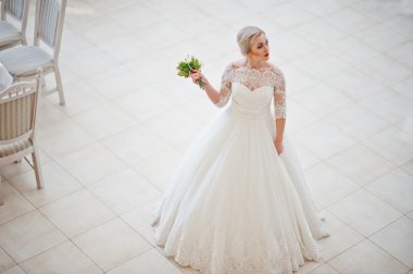 Muhteşem sarışın gelin kapalı büyük düğün salonu poz verdi.