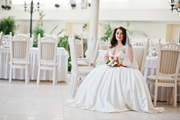 Big breasts brunette bride with wedding bouquet sitting on chair — Stock Photo, Image