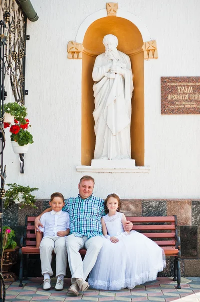 Šťastná rodina na první svaté přijímání sedí na lavičce pozadí — Stock fotografie