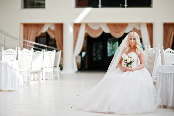 Elegante blond blauwe ogen mode bruid tijdens grote bruiloft zaal sit — Stockfoto