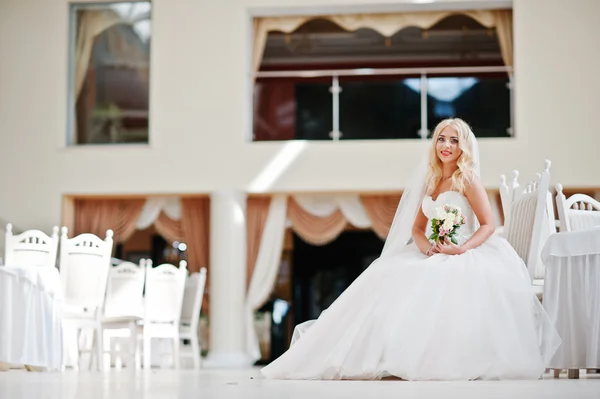 Elegante blond blauwe ogen mode bruid tijdens grote bruiloft zaal sit — Stockfoto