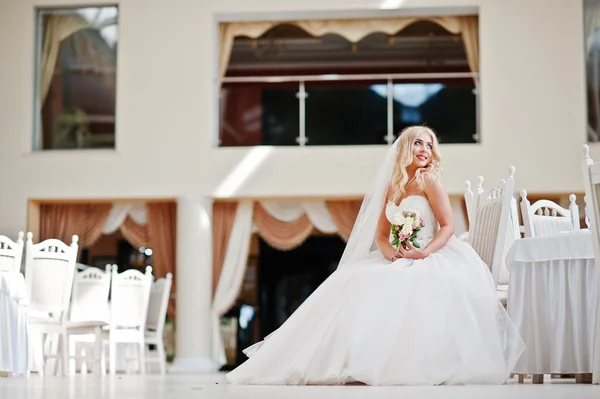 Elegante blond blauwe ogen mode bruid tijdens grote bruiloft zaal sit — Stockfoto