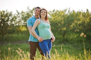 Bahçe magestic günbatımı üzerinde mutlu hamile çifte