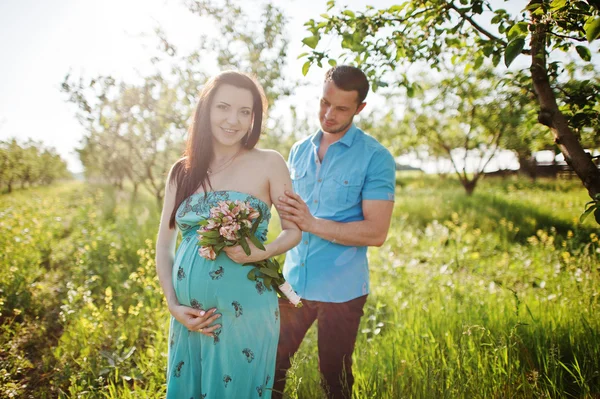 Gelukkige zwangere paar op turquoise jurk op de tuin — Stockfoto