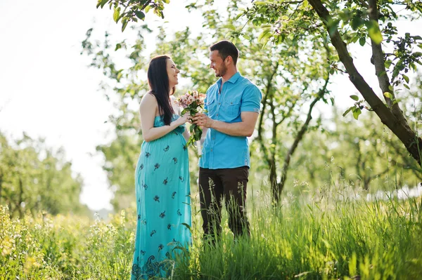 Feliz pareja embarazada en vestido turquesa en el jardín —  Fotos de Stock