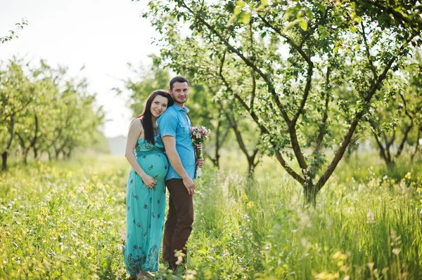 Feliz pareja embarazada en vestido turquesa en el jardín —  Fotos de Stock