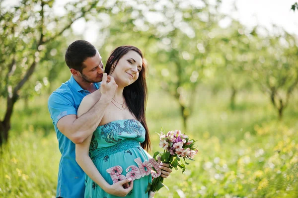 Gelukkige zwangere paar op turquoise jurk op de tuin — Stockfoto