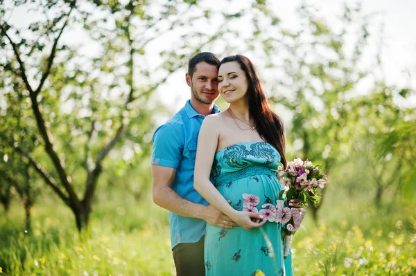 Gelukkige zwangere paar op turquoise jurk op de tuin — Stockfoto