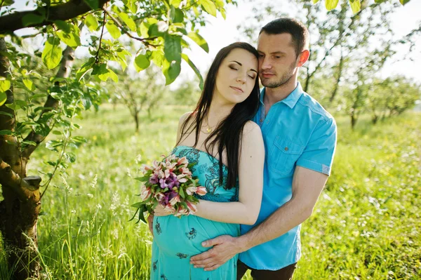 Happy pregnant couple at turquoise dress on the garden — Stock Photo, Image