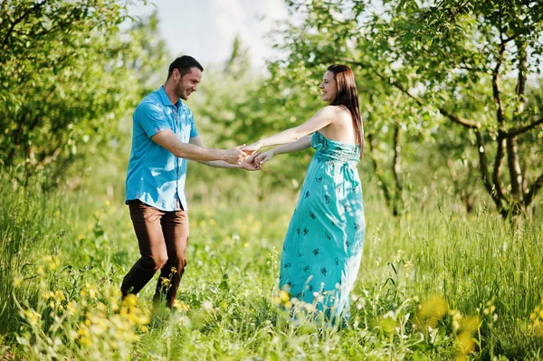 Šťastný pár těhotná v tyrkysové šaty na zahradě — Stock fotografie