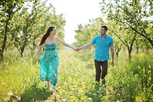 Feliz pareja embarazada en vestido turquesa en el jardín —  Fotos de Stock