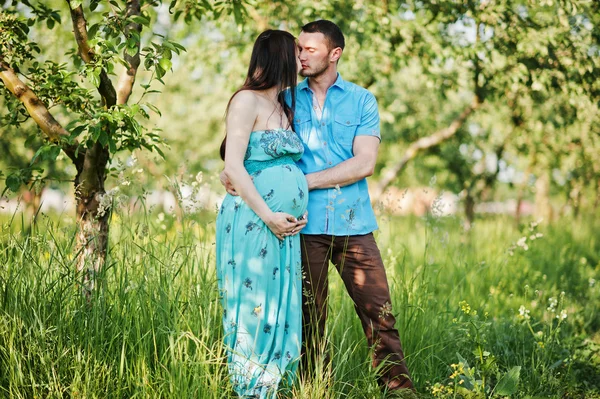 Feliz pareja embarazada en vestido turquesa en el jardín —  Fotos de Stock