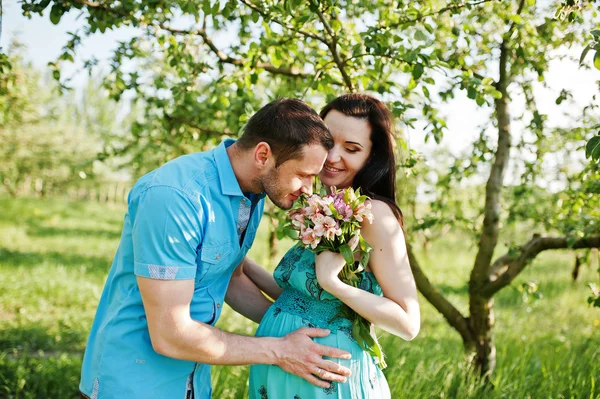 Feliz pareja embarazada en vestido turquesa en el jardín —  Fotos de Stock