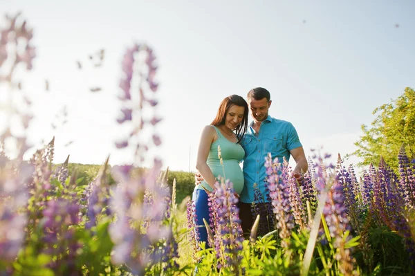 Feliz casal grávida no dia ensolarado perto de flores violetas — Fotografia de Stock