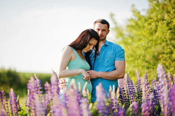 Feliz pareja embarazada en un día soleado cerca de flores violetas —  Fotos de Stock