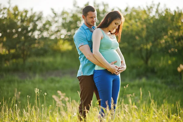 Lyckliga gravida par på garden på väldigt sunset — Stockfoto
