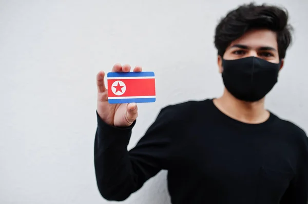 亚洲人戴着全黑面具 手里拿着朝鲜国旗 与白色背景隔离 Coronavirus国家概念 — 图库照片
