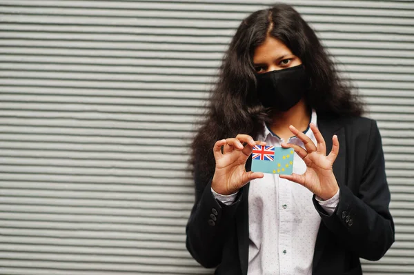 Asian woman at formal wear and black protect face mask hold Tuvalu flag at hand against gray background. Coronavirus at country concept.