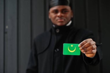 Afrikalı adam siyah durag giyiyor. Moritanya bayrağını elinde tut. İzole edilmiş koyu bir arka plan..