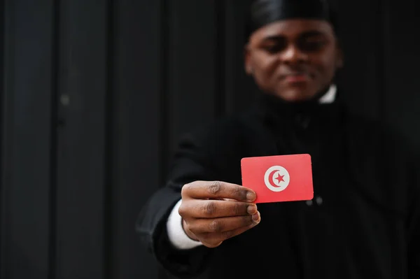 アフリカの男性は黒のデュラグを身に着けていますチュニジアの旗を手で隔離された暗い背景 — ストック写真