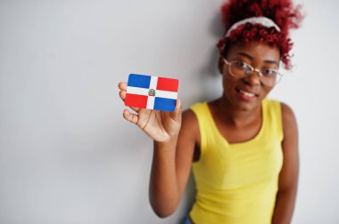 Afro saçlı, sarı cüppeli, gözlüklü, Dominik Cumhuriyeti bayrağını beyaz arka planda tutan Afrikalı Amerikalı kadın..