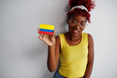 Afro saçlı Afrikalı bir kadın, sarı atlet ve gözlük takıyor, beyaz arka planda Kolombiya bayrağı taşıyor..