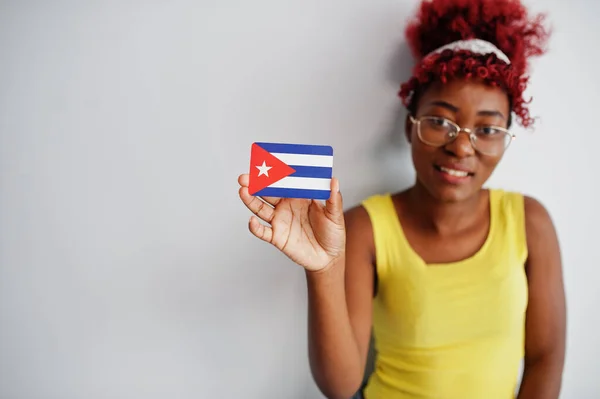アフロヘアのアフリカ系アメリカ人女性 黄色のシングルと眼鏡をかけ 白い背景に孤立したキューバ国旗を保持 — ストック写真